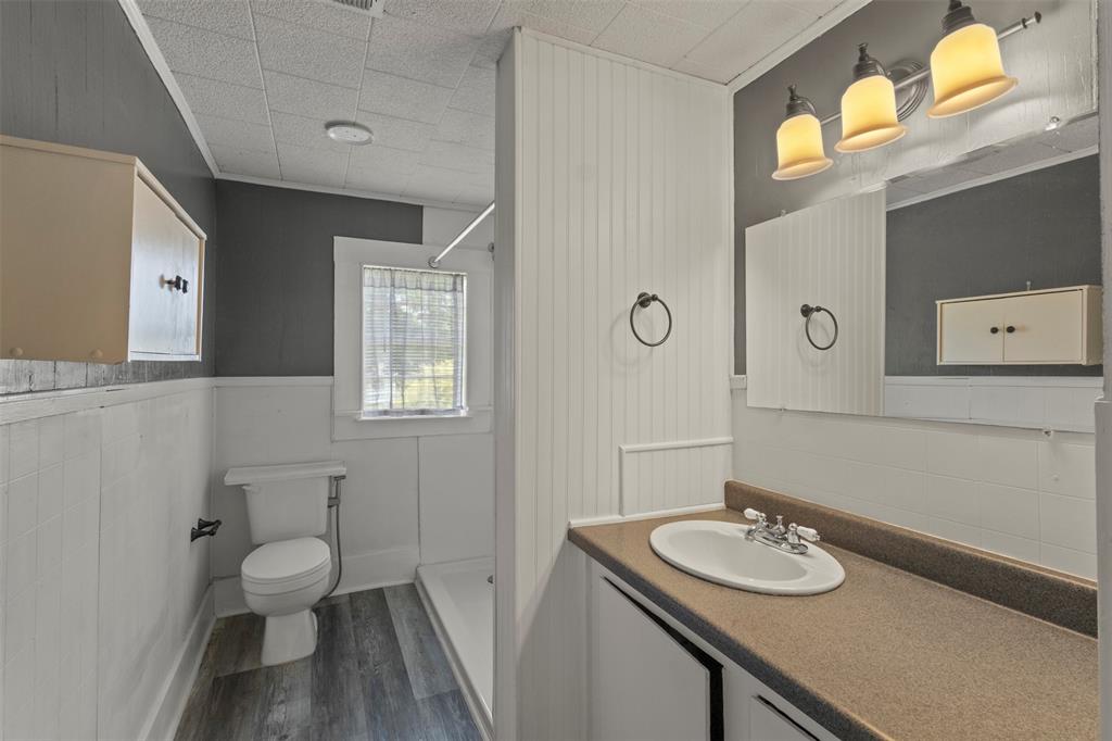 829 West 9th Street Bonham, TX 75418 - Photo 18 of 30 Bathroom featuring a vanity with an integrated sink, a three-light fixture, wood-finish flooring, and white wainscoting