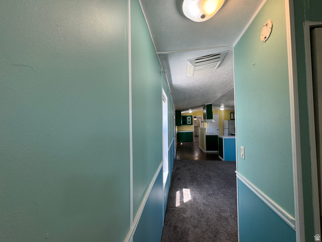 2491 Highway 89, Unit 315 Pleasant View, UT 84404 - Photo 31 of 34 Carpeted hallway with light blue and teal wall paneling, leading into a kitchen with green cabinetry and white appliances