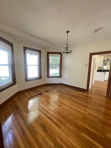 an empty room with wooden floor chandelier and windows
