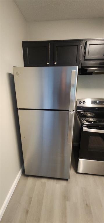18333 Roehampton Drive, Unit 927 Dallas, TX 75252 - Photo 8 of 26 Kitchen featuring stove, freestanding refrigerator, light wood-style flooring, dark cabinetry, and ventilation hood