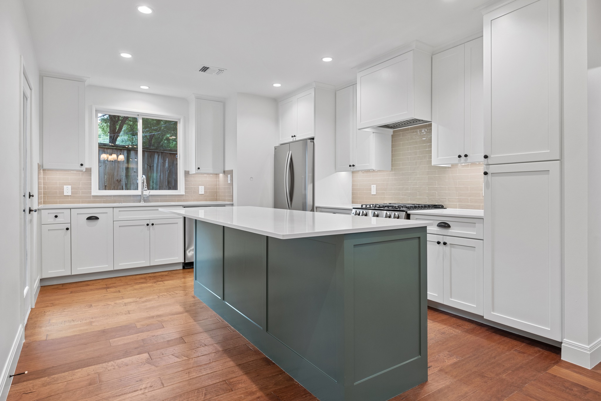 3205 Gilbert Street Austin, TX 78703 - Photo 8 of 35 Modern kitchen featuring a central island with a solid surface countertop, white shaker-style cabinetry, stainless steel appliances, a tiled backsplash, and wood-finish flooring