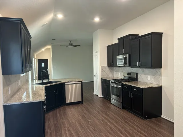 a kitchen with stainless steel appliances granite countertop a stove top oven a sink dishwasher and wooden cabinets with wooden floor