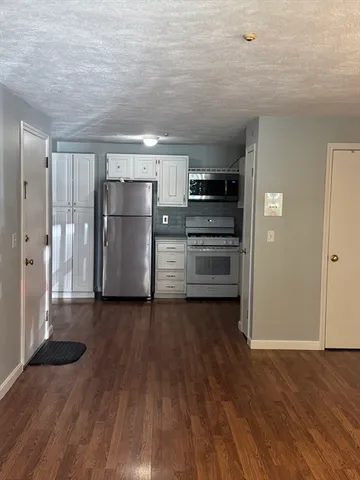 a view of a refrigerator in kitchen and an empty room with wooden floor