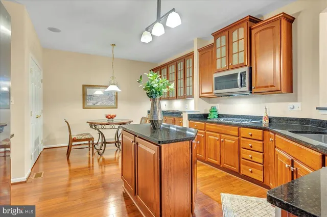 a kitchen with stainless steel appliances granite countertop a stove a sink dishwasher a microwave oven and a dining table with wooden floor