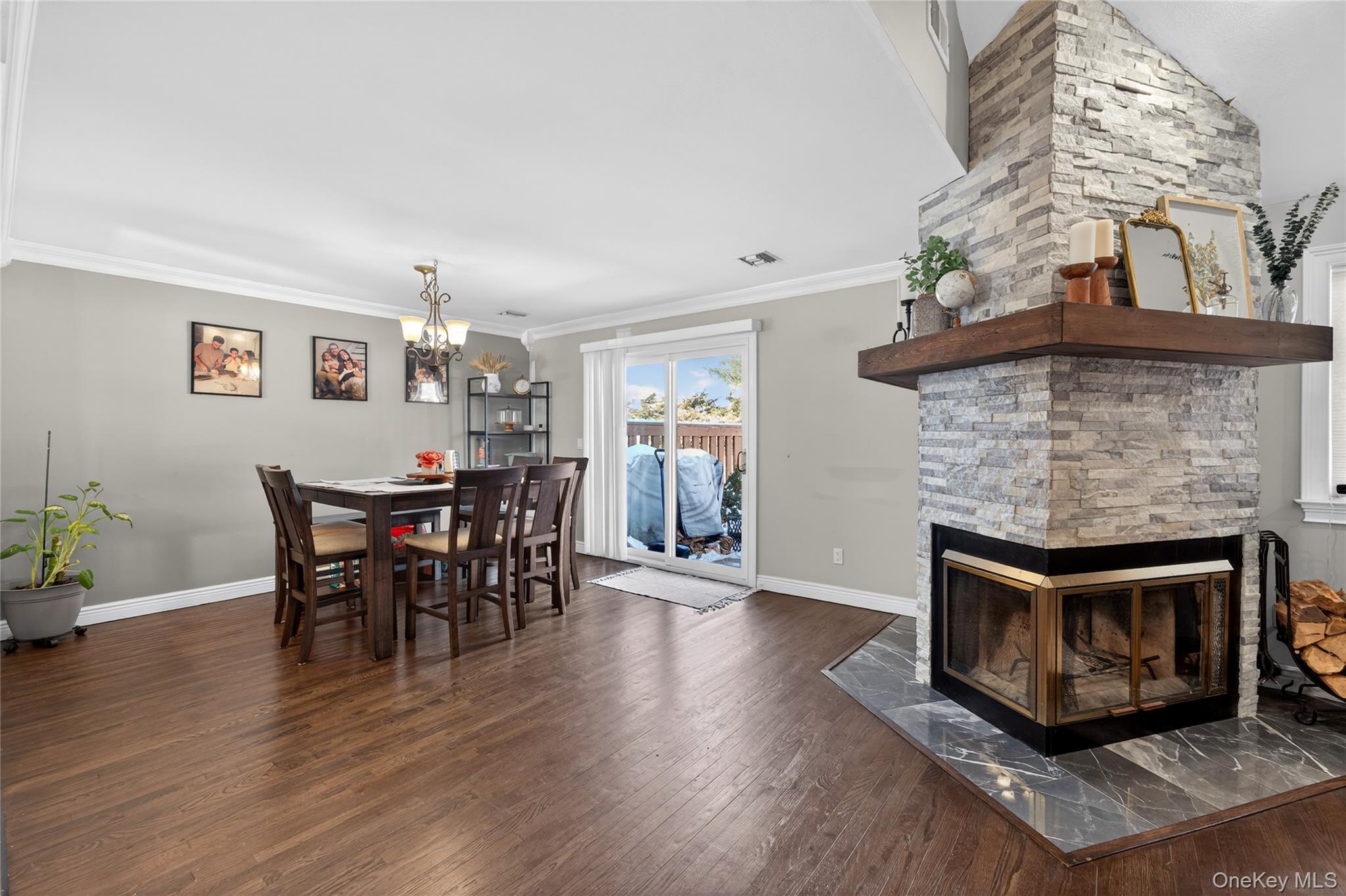 171 Melanie Way Commack, NY 11725 - Photo 5 of 29 Dining area with a stone fireplace, dark wood-style flooring, hanging lights, and crown molding