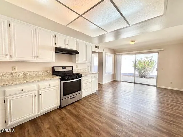 a kitchen with granite countertop a stove top oven a sink and white cabinets with wooden floor