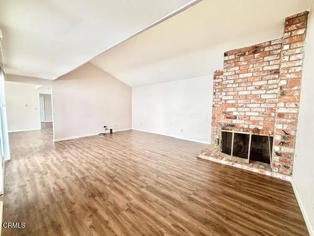 a view of an empty room with wooden floor and a fireplace
