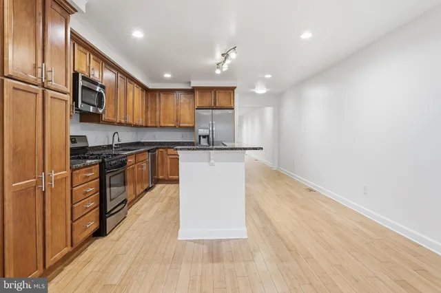 a large kitchen with stainless steel appliances granite countertop a stove a sink dishwasher and a refrigerator with wooden floor