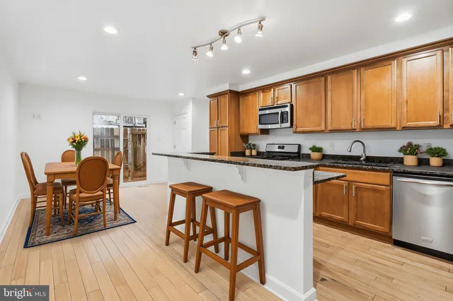 a kitchen with stainless steel appliances granite countertop a stove top oven a sink a dining table and chairs with wooden floor