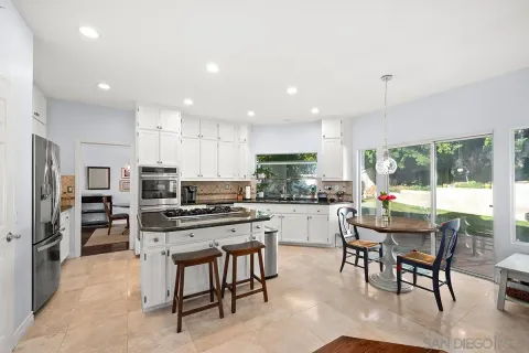 a kitchen with stainless steel appliances kitchen island granite countertop a table chairs microwave and white cabinets