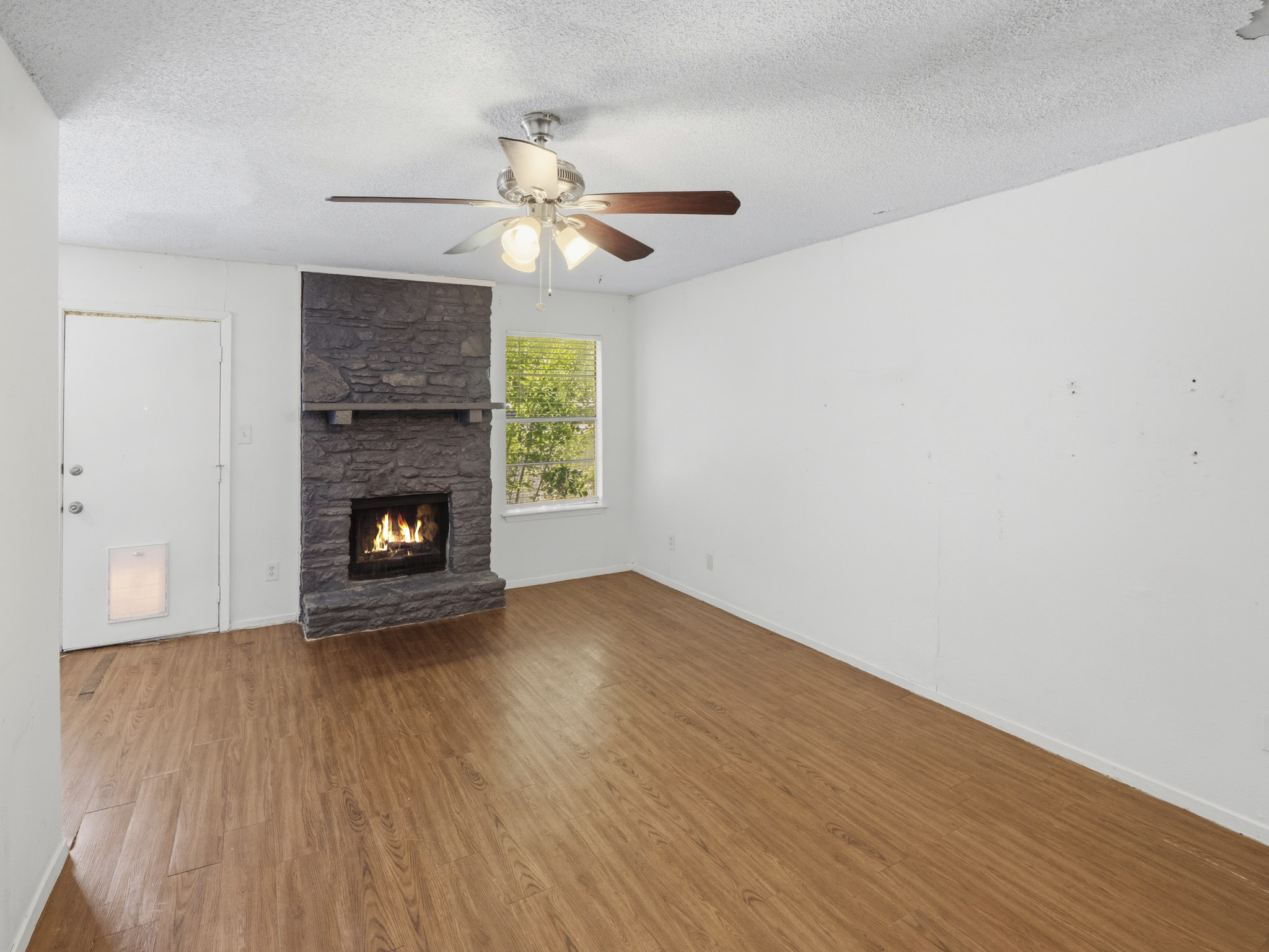 2401 Burleson Road Austin, TX 78741 - Photo 9 of 25 A cozy living space features a stone fireplace, wood-look flooring, and natural light from the window.