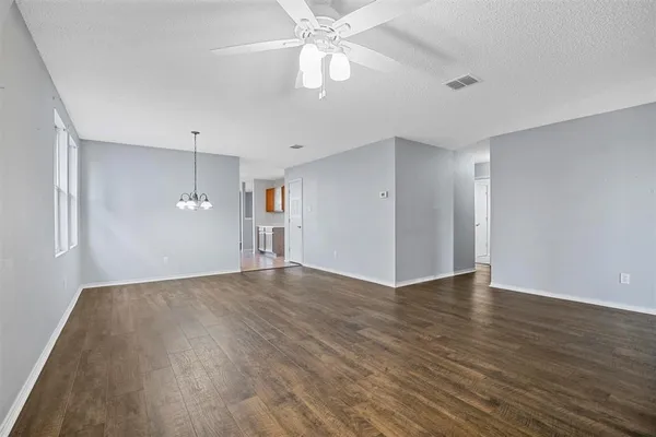 an empty room with wooden floor chandelier fan and windows