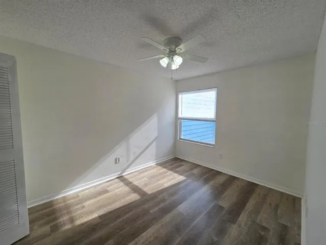 an empty room with wooden floor fan and windows