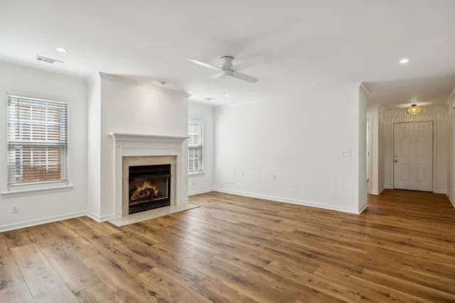 an empty room with wooden floor a fireplace a ceiling fan and windows