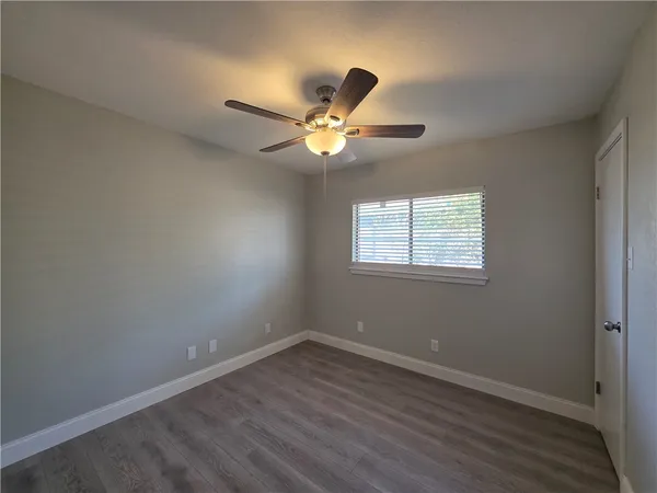 an empty room with wooden floor fan and windows