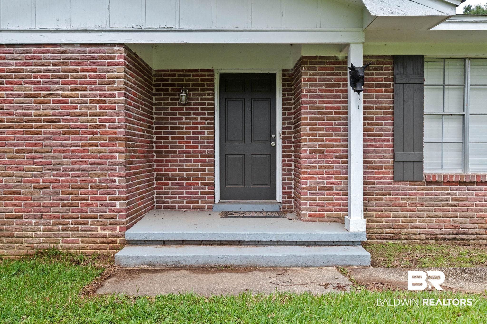384 Old Bratt Road Atmore, AL 36502 - Photo 6 of 64 Brick exterior featuring a covered porch entry, dark paneled front door, white support column, and a decorative wall sconce
