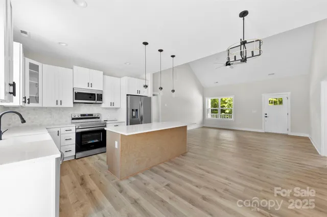 a kitchen with stainless steel appliances granite countertop a stove a sink dishwasher a refrigerator white cabinets and wooden floor