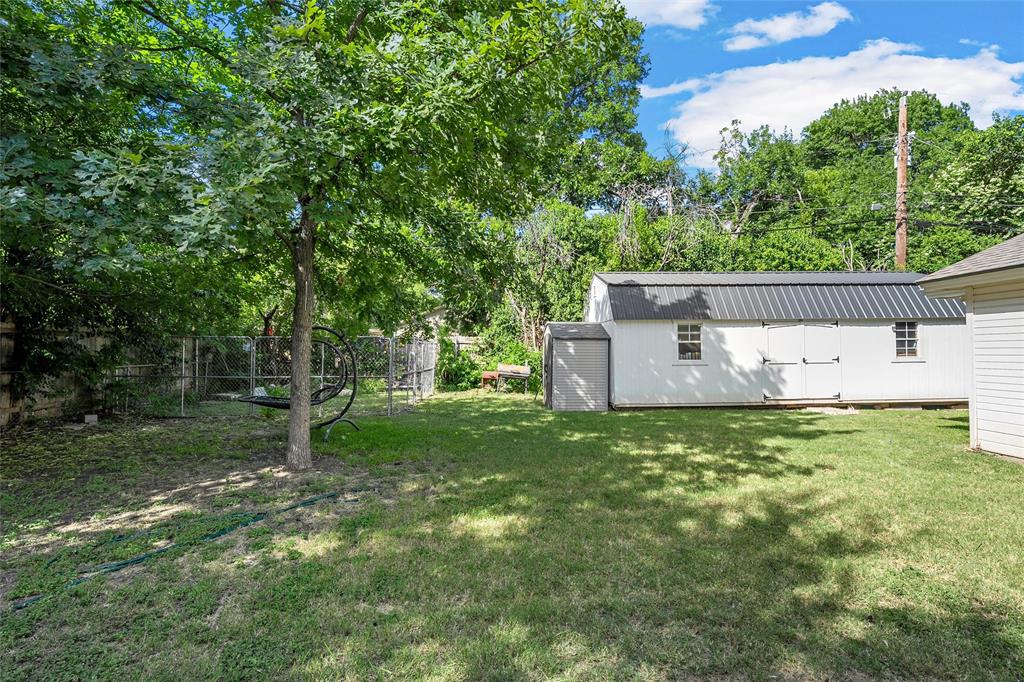 301 North 40th Street Waco, TX 76710 - Photo 25 of 26 Spacious backyard featuring a large white storage building with a dark metal roof, mature trees, and a chain-link fence