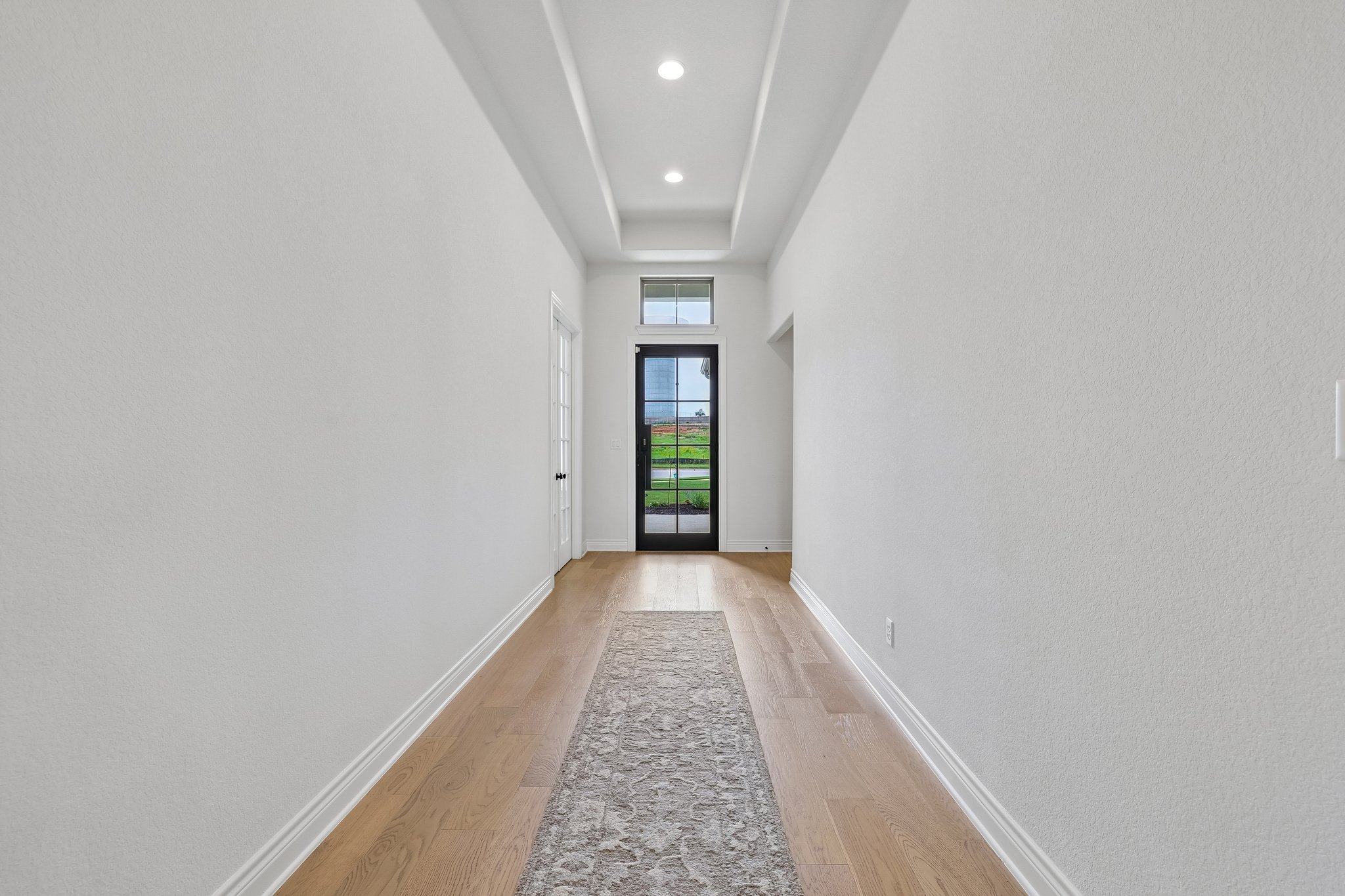 130 Firethorn Loop Bastrop, TX 78602 - Photo 2 of 38 Foyer entry featuring a black multi-pane glass door with transom window, light wood-finish flooring, and a coffered ceiling with recessed lighting