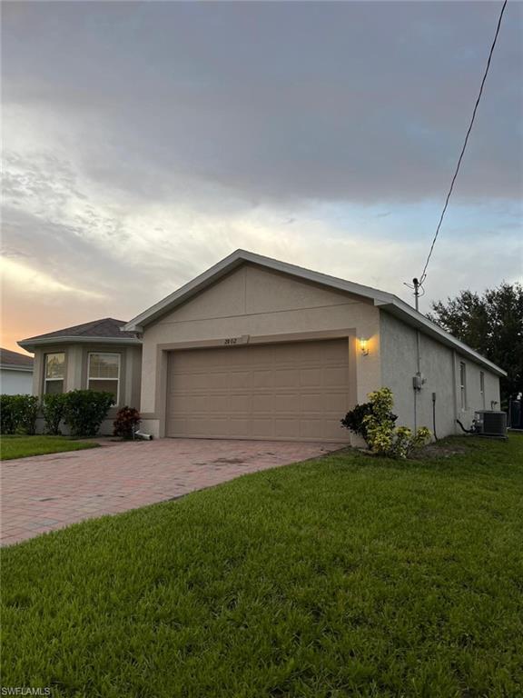 2802 40th Street Southwest Lehigh Acres, FL 33976 - Photo 1 of 14 View of front of house featuring an attached garage, decorative driveway, stucco siding, and a lawn