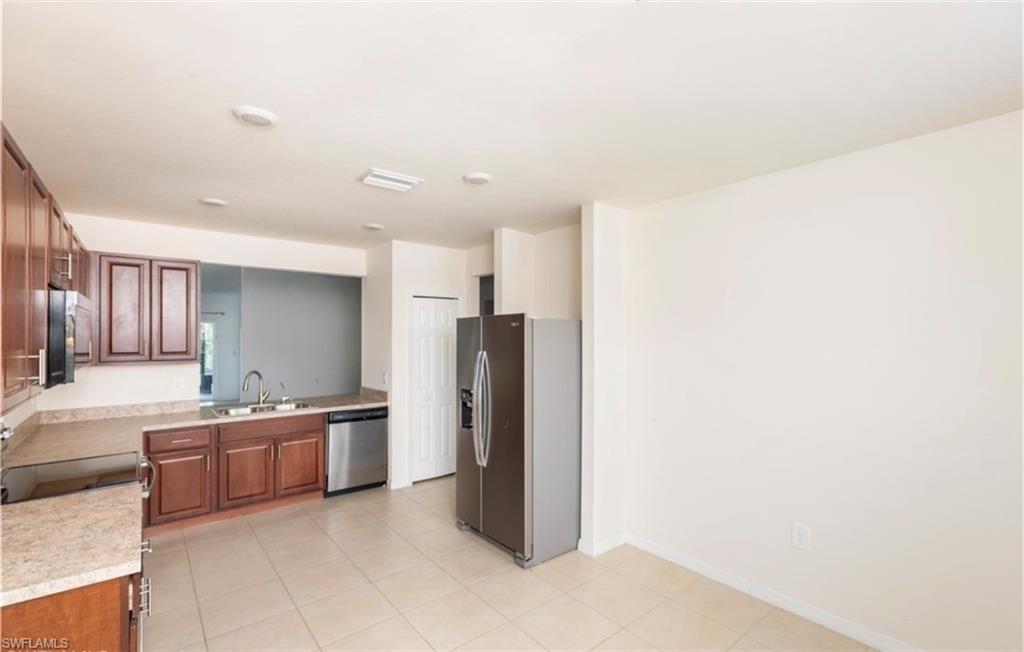 2802 40th Street Southwest Lehigh Acres, FL 33976 - Photo 4 of 14 Kitchen with stainless steel appliances, light countertops, brown cabinetry, and light tile patterned flooring