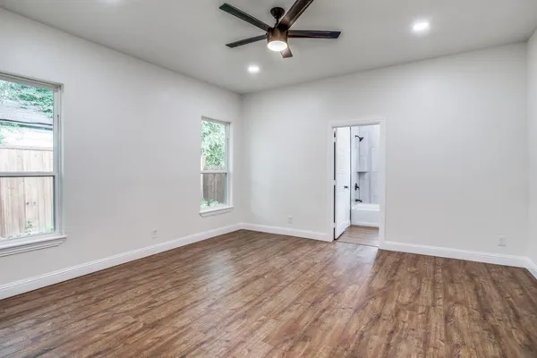an empty room with wooden floor a ceiling fan and windows
