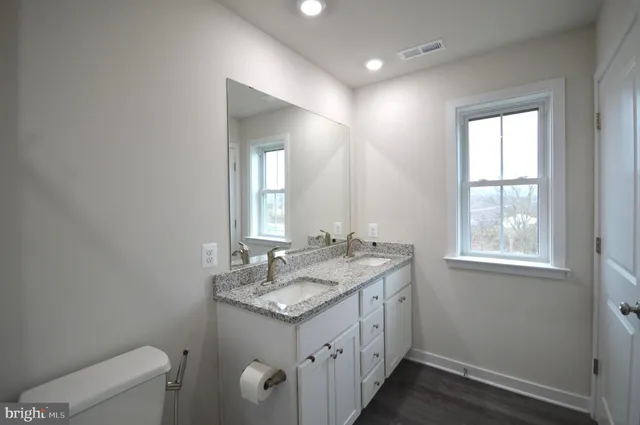 a bathroom with a granite countertop sink a toilet and a window