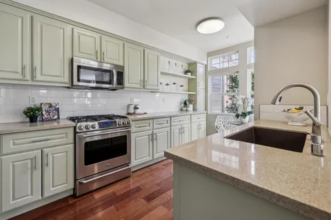 a kitchen with stainless steel appliances white cabinets a sink a stove a microwave and wooden floors