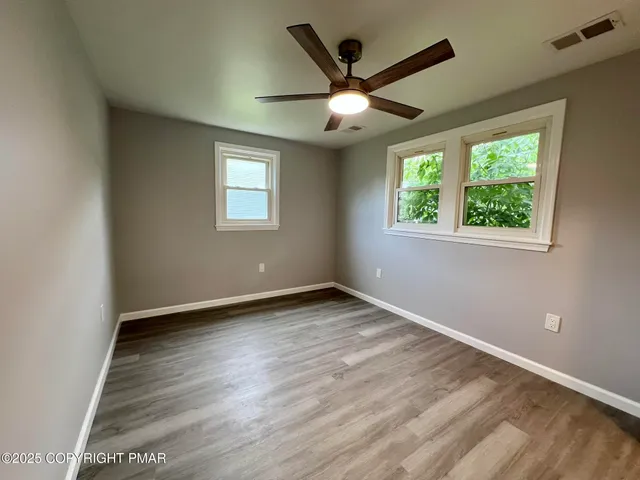 an empty room with wooden floor fan and windows