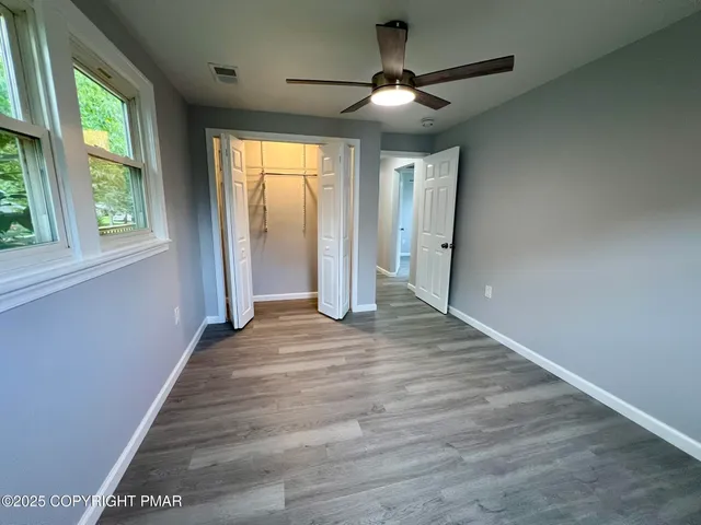 an empty room with wooden floor fan and windows
