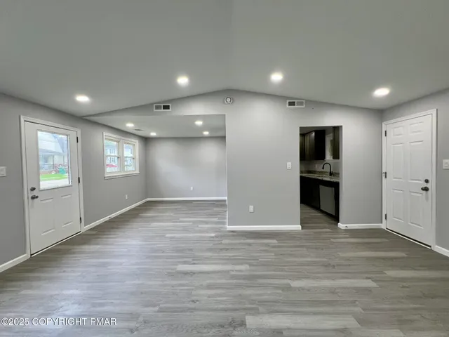 a view of empty room with wooden floor and kitchen