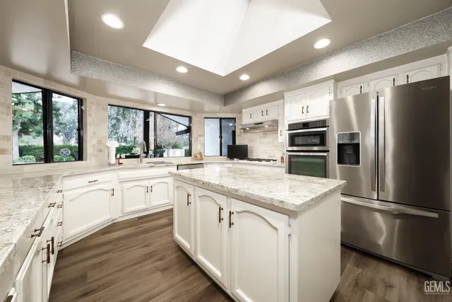 a kitchen with stainless steel appliances granite countertop a refrigerator a sink dishwasher a stove and white countertops with wooden floor