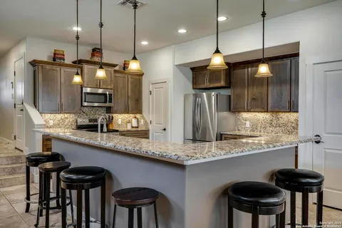 a kitchen with stainless steel appliances granite countertop a sink a refrigerator a stove a kitchen island and chairs