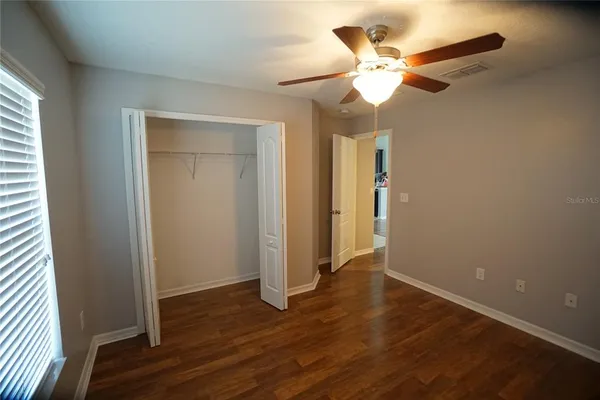 an empty room with wooden floor fan and windows
