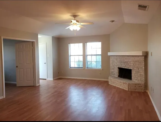 an empty room with wooden floor fireplace and windows