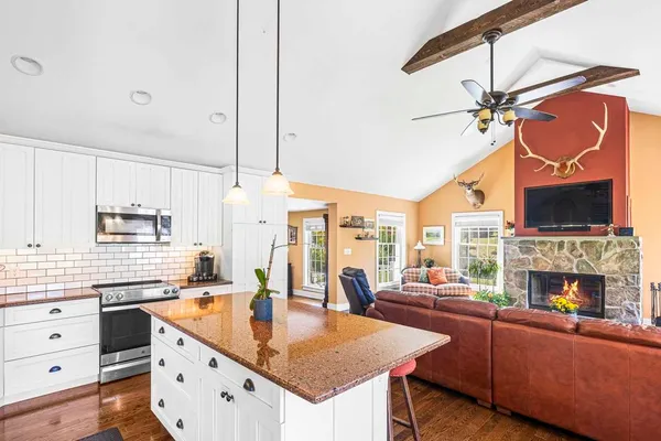 a living room with stainless steel appliances kitchen island granite countertop furniture a fireplace and a chandelier