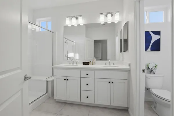 a bathroom with a double vanity sink a toilet a shower and a mirror