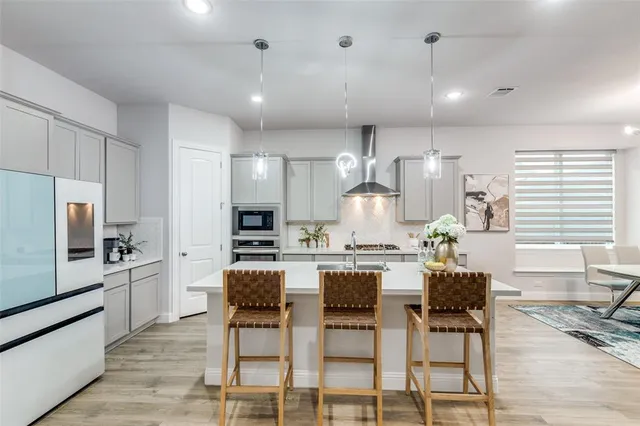 a kitchen with stainless steel appliances kitchen island granite countertop a stove a refrigerator a oven a sink with white cabinets and chairs