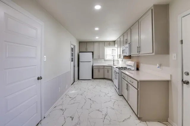 a kitchen with granite countertop a refrigerator a sink and white cabinets