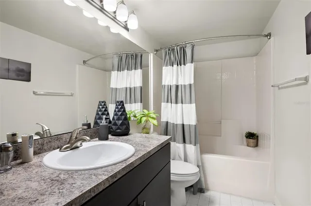 a bathroom with a granite countertop sink a toilet a mirror a bathtub and shower