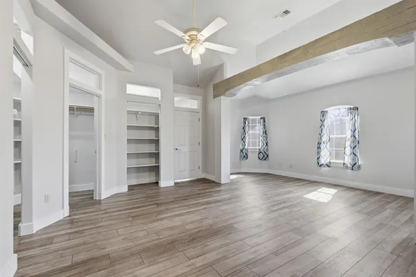 an empty room with wooden floor chandelier fan and windows