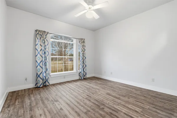 an empty room with wooden floor and windows with curtains