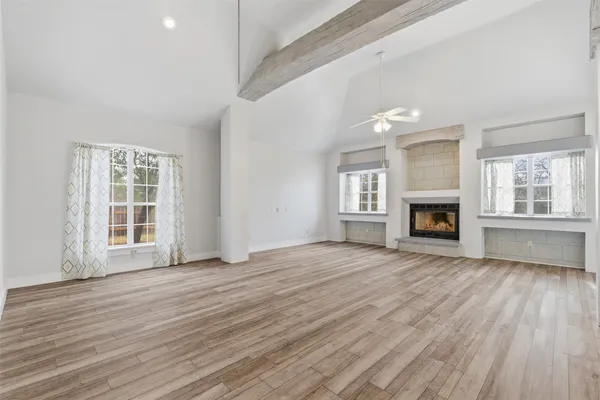 an empty room with wooden floor fireplace and windows
