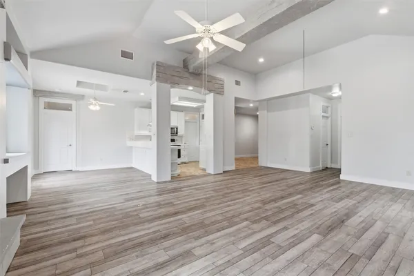 a view of an empty room with wooden floor and a ceiling fan