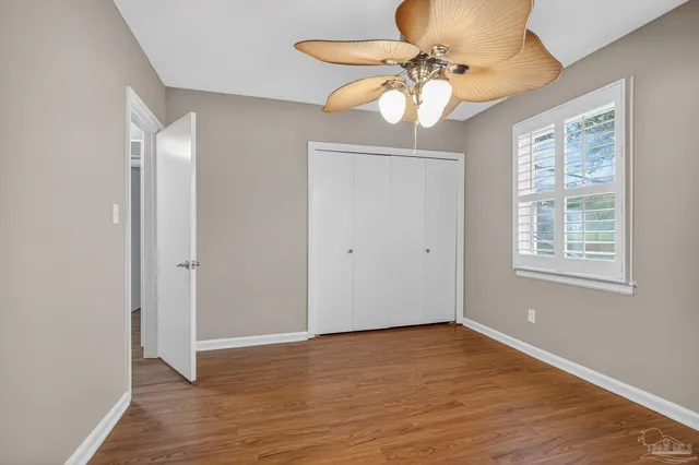 an empty room with wooden floor windows and fan