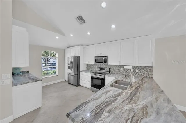 a kitchen with stainless steel appliances granite countertop a stove top oven a sink dishwasher a dining table and chairs with wooden floor