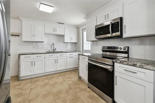 a kitchen with stainless steel appliances granite countertop a sink a stove top oven and white cabinets