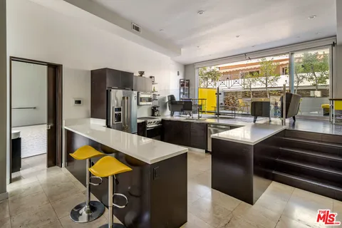 a kitchen with stainless steel appliances kitchen island granite countertop a refrigerator a stove and a dining table with wooden floor