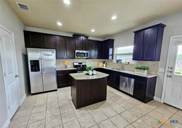 a kitchen with kitchen island granite countertop a stove a refrigerator and a sink with wooden cabinets