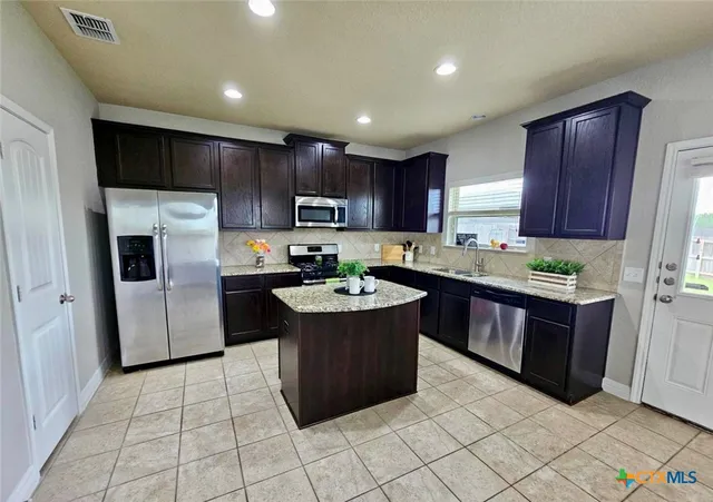 a kitchen with kitchen island granite countertop a stove a refrigerator and a sink with wooden cabinets